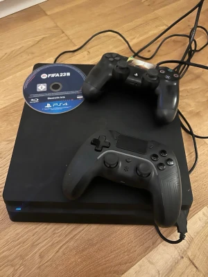 PlayStation 4 med två handkontroller - Svart PlayStation 4 Pro med två handkontroller, en original DualShock 4 och en extra kontroll. FIFA 23-skiva för PS4 ingår. .