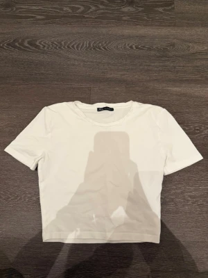 Vit croppad t-shirt från Zara - En enkel och stilren vit croppad t-shirt från Zara. T-shirten har korta ärmar och rund halsringning. Perfekt basplagg att matcha med allt och tillverkad i mjuk bomull för skön känsla.