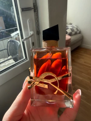 Yves Saint Laurent Libre Le Parfum 50ml - Säljer en ikonisk parfym från Yves Saint Laurent, Libre Eau de Parfum. Flaskan är rektangulär i genomskinligt glas med bärnstensfärgad vätska och har en elegant svart asymmetrisk kork samt en guldig YSL-logga runt flaskan. Lyxig och modern design som sticker ut i badrumshyllan.