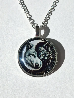 Halsband med yin yang vargmotiv - Snyggt halsband med runt hängsmycke i metall och i 2D Retro mode. Motivet visar två vargar i yin yang-stil, en ljus och en mörk, vilket ger en cool kontrast. Kedjan är silverfärgad och har klassisk länkkedja. Materialet rostfritt stål. 