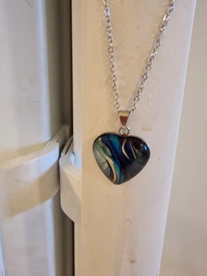Halsband med hjärthänge - Snyggt halsband med silverfärgad kedja och ett hjärtformat hänge med glasöverdrag. Hänget har ett motiv i olika färger. Kedja 45 + 5 cm. Berlock 2 × 2 cm.