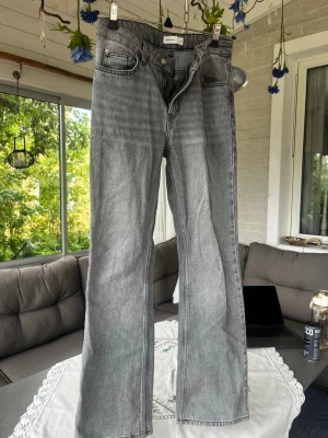 Grå raka jeans från Gina Tricot - Säljer ett par grå jeans från Gina Tricot med rak passform och klassisk femficksdesign. Jeansen har hög midja, bälteshällor och är tillverkade i ett slitstarkt denimtyg. Perfekta för en avslappnad och trendig look. Jeansen är lite slitna vid byxkanten