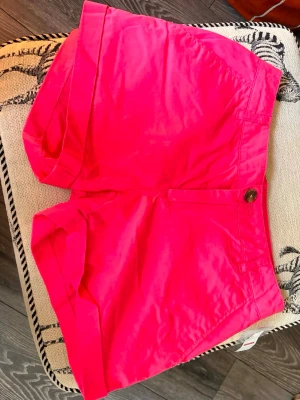 Rosa shorts med knapp framtill - Snygga rosa shorts med klassisk passform och knapp framtill. De har fickor på sidorna och är perfekta för varma sommardagar. Stilen är enkel och fräsch, och materialet känns lätt och bekvämt.