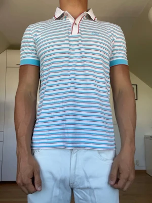 Randig pikétröja från BOSS - Randig vit, blå och röd piké från Boss. Den sitter som en strl S/M. Inga defekter. Modellen är 178 cm och väger 77 kg. Hör gärna av dig vid frågor!