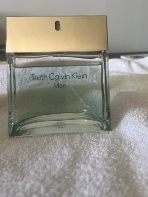 Truth Calvin Klein Men Eau de Toilette - Fräsch herrparfym från Calvin Klein, Truth Men, i en stilren glasflaska med guldigt lock. Flaskan rymmer ca 90% av 100 ml och har en modern, transparent design. Perfekt för dig som gillar eleganta och klassiska dofter.