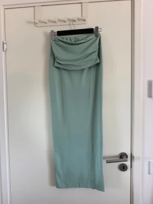 Mint långkjol med tubtopp - Snygg mint långkjol med en tubtopp med draperad midja och rak passform. Kjolen har en enkel och stilren design som ger en modern look. Perfekt att matcha med en crop top eller en enkel t-shirt för en trendig outfit. Stygnen nere i kjolen har gått upp, går att sy eller om man vill dra upp den går de bra också. Använd två gånger.