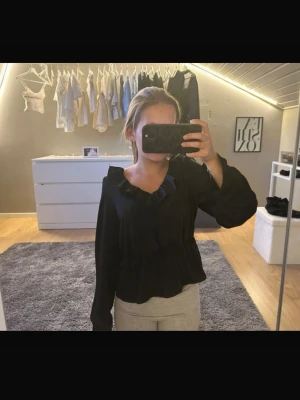Svart volangblus - Svart blus med volangdetaljer vid halsringningen och nedtill. 💕 Långärmad modell med lös passform och breda muddar vid ärmsluten. Perfekt att styla med jeans eller kjol för en trendig look. 😚 Köpt på Vero Moda för 400kr
