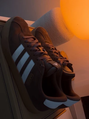 Adidas sneakers brun/mocka-look - Säljer ett par snygga Adidas sneakers i brun färg med vita ränder och gummisula. Använda knappt så är  fortfarande i mycket fint skick. Bekväma och passar till det mesta. Är i US 9 1/2