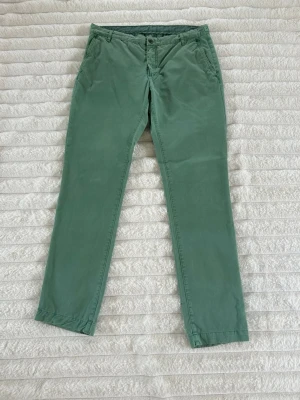 Gröna chinos från Tiger of Sweden - Snygga gröna chinos från Tiger of Sweden i klassisk rak modell. Byxorna har sidfickor och är tillverkade i ett mjukt bomullstyg med lite stretch för extra komfort. Perfekta för en stilren och avslappnad look.