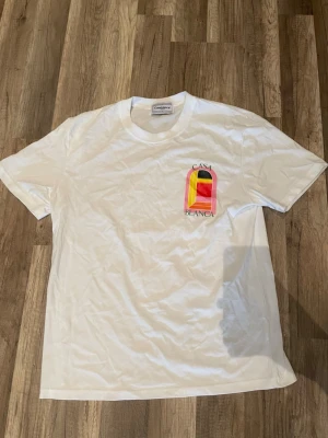 Vit t-shirt från Casablanca - ALLA PRISFÖRSLAG ACCEPTERAS Vit t-shirt från Casablanca med färgglad grafisk detalj och texten 'Casa Blanca' på bröstet. Klassisk rund hals och korta ärmar. Perfekt för dig som gillar stilrena plagg med en twist.ALLA PRISFÖRSLAG ACCEPTERAS 