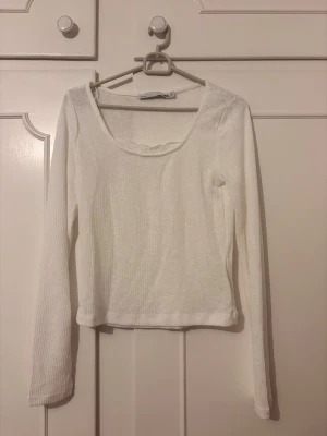 Vit ribbad långärmad topp - En enkel och stilren vit ribbad topp med lång ärm och rundad urringning. Perfekt att matcha med jeans eller kjol för en clean look. Materialet är mjukt och stretchigt för extra komfort.