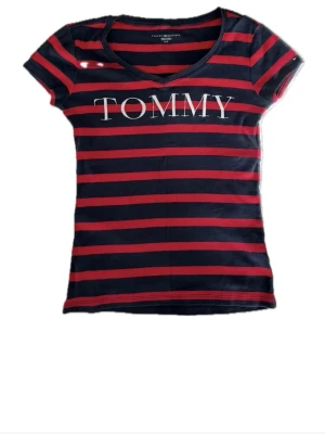 Figurformad Tommy Hilfiger topp - Fin figurformad T-shirt från Tommy Hilfiger. Snygg passform. Storlek S men stretchigt tyg. Blå och röd randig med broderade bokstäver. 