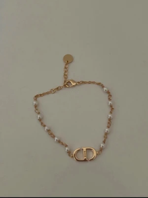  armband med pärlor och guld - Snyggt armband med guldfärgad kedja och små vita pärlor. Armbandet har ett klassiskt i mitten och justerbar längd med en rund bricka vid låset. Perfekt accessoar för dig som gillar lyxiga detaljer och elegant design.
