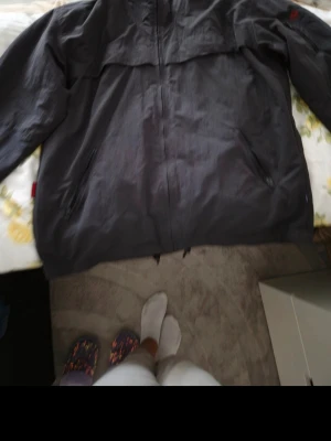 Svart vindjacka från Fjällräven - Snygg svart vindjacka från Fjällräven med dragkedja framtill och två sidofickor med dragkedja. Jackan har en diskret röd Fjällräven-logga på bröstet och är tillverkad i ett lätt och slitstarkt material, perfekt för blåsiga dagar.