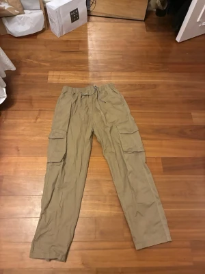 Beiga cargobyxor med fickor - Snygga beiga cargobyxor med flera stora fickor på sidorna och elastisk midja med dragsko. Perfekta för en avslappnad och trendig stil. Tillverkade i ett lätt och bekvämt material som passar året runt.