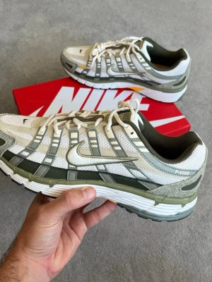 Nike P-6000 sneakers i beige och oliv - Nike P-6000 sneakers i mesh och syntetmaterial med beige, olivgröna och vita detaljer. Skorna har en chunky sula med inslag av gult och svart, samt klassisk Nike Swoosh på sidan. Perfekta för dig som gillar retrovibbar och streetwear.