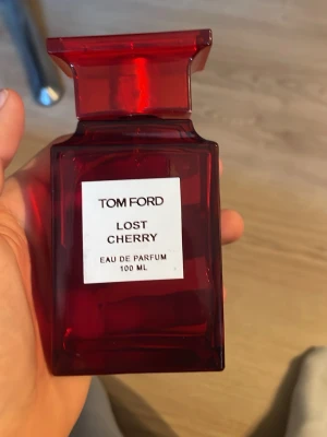Tom Ford Lost Cherry 100 ml parfym - Tom Ford Lost Cherry Eau de Parfum i en lyxig, mörkröd glasflaska på 100 ml. Flaskan har en elegant, fyrkantig form och tydlig etikett framtill. Doften är känd för sina söta och fruktiga toner med inslag av körsbär.