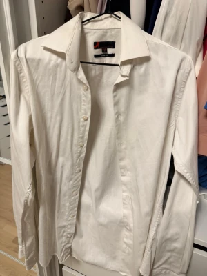 Vit slim fit skjorta S - Klassisk vit skjorta i slim fit-modell med långa ärmar och knappar framtill. Skjortan har en stilren design och är tillverkad i ett mjukt bomullstyg som passar perfekt till många olika looks.