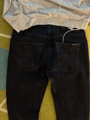 Nudie Jeans - Säljer ett par svarta jeans från Nudie Jeans med klassisk femficksmodell och raka ben. Jeansen har snygga sömdetaljer på bakfickorna och är tillverkade i mjuk denim. Perfekta för dig som gillar stilrena och tidlösa plagg. Storleken är 32/32 modell: Grim Tim