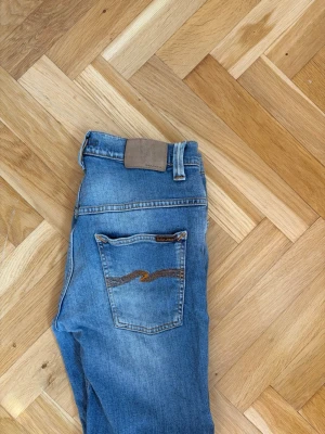 Nudie jeans  - Säljer ett par klassiska nudie jeans med rak passform och kontrastsöm på bakfickan. Jeansen har fem fickor, bälteshällor och en snygg tvättad look. Perfekta till vardags och passar till det mesta. Materialet är denim i bomull.