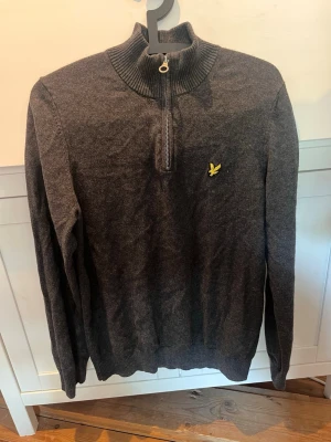 Lyle & Scott halvzip stickad tröja - Snygg mörkgrå långärmad tröja med halv dragkedja och ribbad krage från lyle & scott. Perfekt för höst och vinter. Buda gärna. 