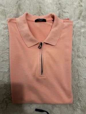 Ljusrosa polotopp med dragkedja - Säljer en ljusrosa polotopp från Jack & Jones med korta ärmar och en snygg dragkedja framtill. Toppen har klassisk krage och är gjord i mjukt bomullsmaterial. Perfekt för dig som gillar stilrena och bekväma plagg.
