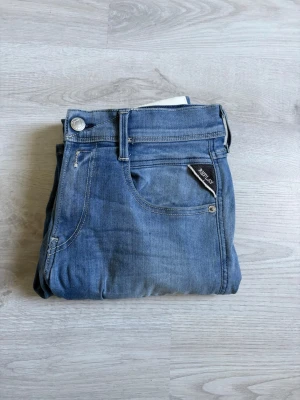 Blå raka jeans från Replay - Säljer ett par klassiska blå jeans från Replay med raka ben och fem fickor. Jeansen har en snygg tvättad look och silverfärgade detaljer vid fickorna. Perfekta för dig som gillar en avslappnad men stilren stil.