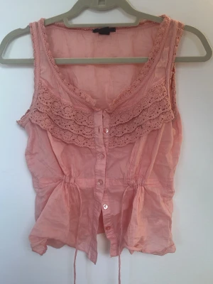 Rosa spetsdetaljerad linnetopp - Söt rosa linnetopp med knappar, inga defekter/hål. säljer därför att den ej kommer till anvöndning. passar jätte bra med en tshirt eller en långärmad tröja under❣️ passar xs-s