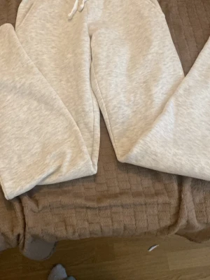 Ljusgrå mjukisbyxor från Gina Tricot - Mysiga ljusgrå mjukisbyxor från Gina Tricot med dragsko i midjan och ribbad kant upptill. Tillverkade i mjukt bomullsmaterial som känns skönt mot huden. Perfekta för chill dagar hemma eller när du vill vara bekväm.