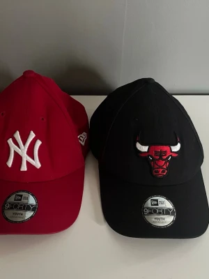 New Era kepsar NY & Bulls Youth - Två snygga New Era 9FORTY kepsar i youth-storlek. En röd med vit New York Yankees-logga och en svart med Chicago Bulls-logga i rött och vitt. Båda är böjda i skärmen och tillverkade i 100% bomull. Perfekta för dig som gillar sportig streetstyle.