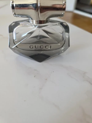Gucci Bamboo Eau de Parfum - Gucci Bamboo Eau de Parfum i en elegant, transparent glasflaska med silverfärgat lock. Flaskan har en unik, diamantliknande form och stilren design med GUCCI-loggan tryckt på framsidan. Perfekt för dig som gillar exklusiva och lyxiga dofter.