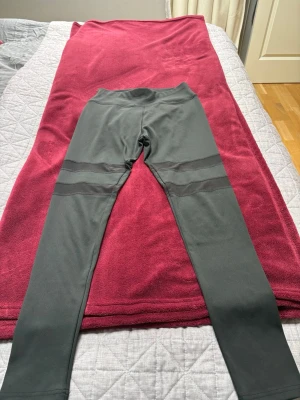 Mörkgrå leggings med meshdetaljer - Snygga mörkgrå leggings med transparenta meshpaneler ovanför knäna. Hög midja och tight passform som ger en sportig look. Perfekta för träning eller chill. Materialet känns stretchigt och bekvämt.
