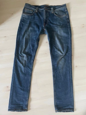 Ljusblå Nudie slim fit jeans - Snygga blå/ljusblå slim fit jeans från Nudie  med klassisk femficksdesign Jeansen har normal midja och raka ben. Tillverkade i denim med en skön stretch för extra komfort. Storlek W 34 L 32 Modellen är Lean Dean och är slim/straight