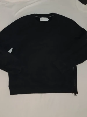 Calvin Klein sweatshirt - Säljer en svart sweatshirt från Calvin Klein Jeans med rund halsringning och diskret logotyp på bröstet. Tröjan har långa ärmar och ribbade muddar vid ärmslut och nederkant. Perfekt för en stilren och avslappnad look.