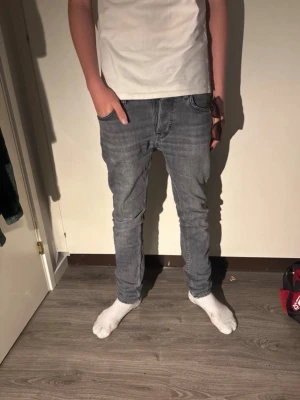 Mörkgrå Nudie Jeans Slim Fit - Säljer ett par mörkgrå slim fit jeans från Nudie Jeans. Klassisk femficksmodell med den ikoniska vågade sömmen på bakfickan. Jeansen har normal midja och är tillverkade i mjuk denim, perfekta för en avslappnad och stilren look.