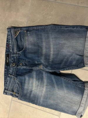 Blå jeansshorts från Replay - Snygga blå jeansshorts från Replay med klassisk femficksdesign och uppvikta benslut. Shortsen har en normal passform och stängs med knappar framtill.