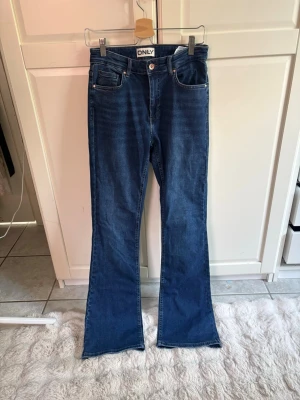 Blå bootcut jeans från ONLY - Säljer ett par snygga blå bootcut jeans från ONLY i storlek L/34. Jeansen har klassisk femficksdesign, hög midja och utsvängda ben. Perfekta för dig som gillar en retroinspirerad look och vill ha ett par jeans som sticker ut lite extra. Aldrig använda