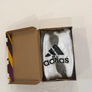 Vita Adidas Ultra Boost sneakers - Snygga helvita Adidas Ultra Boost sneakers med stickad ovandel och klassiska tre ränder på sidan. Skorna har en tjock, responsiv sula och en sportig siluett. Perfekta för dig som gillar stilrena och bekväma sneakers med modern känsla.