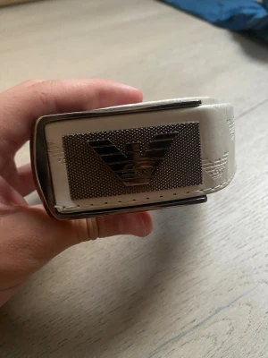 Vitt bälte med stor metallspänne - Snyggt vitt bälte med präglade loggor och ett stort, rektangulärt metallspänne framtill. Bältet har en clean look och passar perfekt till jeans eller byxor för att lyfta din outfit.