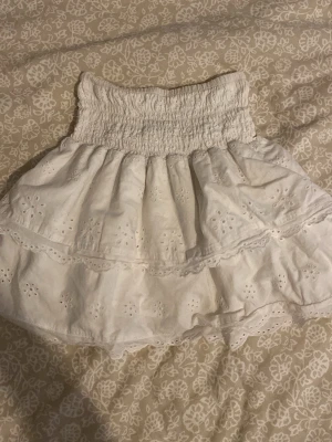 Vit volangkjol från H&M - Supersöt vit kortkjol från H&M med broderade detaljer och volanger. Kjolen har smock i midjan för en bekväm passform och är gjord i bomull. Perfekt för varma dagar och ger en romantisk vibe till din outfit. Storleken är 152 men den passar xs, s, och m då den är stretchig 