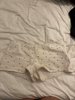 Vita prickiga shorts från Zara - Säljer ett par vita shorts med svarta prickar. De har en enkel och rak passform med korta ben och är tillverkade i ett mjukt bomullstyg. Perfekta för varma dagar och ger en söt och avslappnad look. Helt oanvända men ingen prislapp kvar. Slutsålt på hemsida. Är i storlek 36 men passar på mig som brukar ha 34
