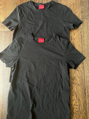Svarta t-shirts från Hugo - Två stilrena svarta t-shirts från Hugo med klassisk rund halsringning och korta ärmar. Perfekta till jeans eller shorts för en clean och enkel look. Tillverkade i mjukt material som känns skönt mot huden.