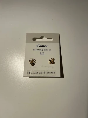 Örhängen i guldpläterat silver - Snygga örhängen från Glitter i form av rosesmå hjärtan. Tillverkade i sterling silver 925 och pläterade med 18 karat guld. Perfekta för dig som gillar stilrena och trendiga accessoarer med guldfinish. Oanvända.