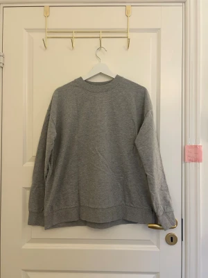 Grå sweatshirt från 157 - En basic grå sweatshirt från 157 med rund halsringning och ribbade muddar vid ärmslut och nederkant. Tillverkad i mjukt material som passar perfekt till chill dagar eller när du vill ha en enkel och clean look. Klassisk modell utan tryck eller detaljer.