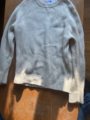 Beige stickad tröja från NN07 - Stickad tröja i beige från NN07 med rund halsringning och ribbstickad struktur. Tröjan har långa ärmar och breda muddar vid ärmslut och nederkant. Perfekt för lager på lager och enkel att matcha med olika stilar.