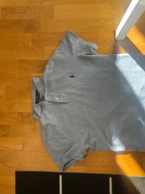 Ljusgrå pikétröja från Polo Ralph Lauren - Snygg ljusgrå pikétröja från Polo Ralph Lauren med klassisk krage, två knappar och broderad logga på bröstet. Modellen är Custom Slim Fit och passar perfekt till en avslappnad men stilren look.