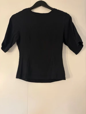 Svart topp med korta ärmar - En enkel svart topp med rund hals och halv långa ärmar. Modellen är figurnära och har en klassisk, stilren look som passar till det mesta. 