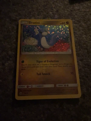 Dratini Pokémonkort holo - Säljer ett holografiskt Dratini Pokémonkort med gul ram och färgglad bakgrund. Kortet har motiv av Dratini och text på engelska. Perfekt för samlare eller Pokémonfans som vill utöka sin kortsamling.