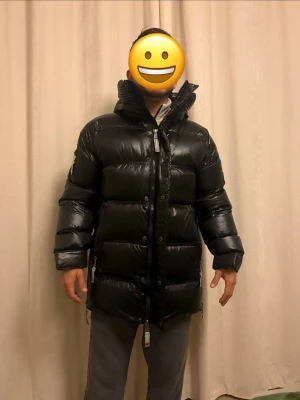Svart lång dunjacka från CAYA - Säljer en svart, glansig och lång dunjacka från CAYA med hög krage och huva. Köpte den för 6.500kr förra året, aldrig använt. Modellen är 1,72 76kg