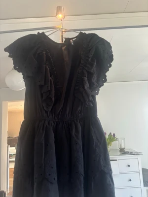 Svart volangklänning med broderi - Säljer en svart kortklänning med volangdetaljer och broderade mönster. Klänningen har korta ärmar med volanger och en luftig passform. Perfekt för dig som gillar romantiska detaljer och en feminin look. Aldrig använd men prislapp borttagen 